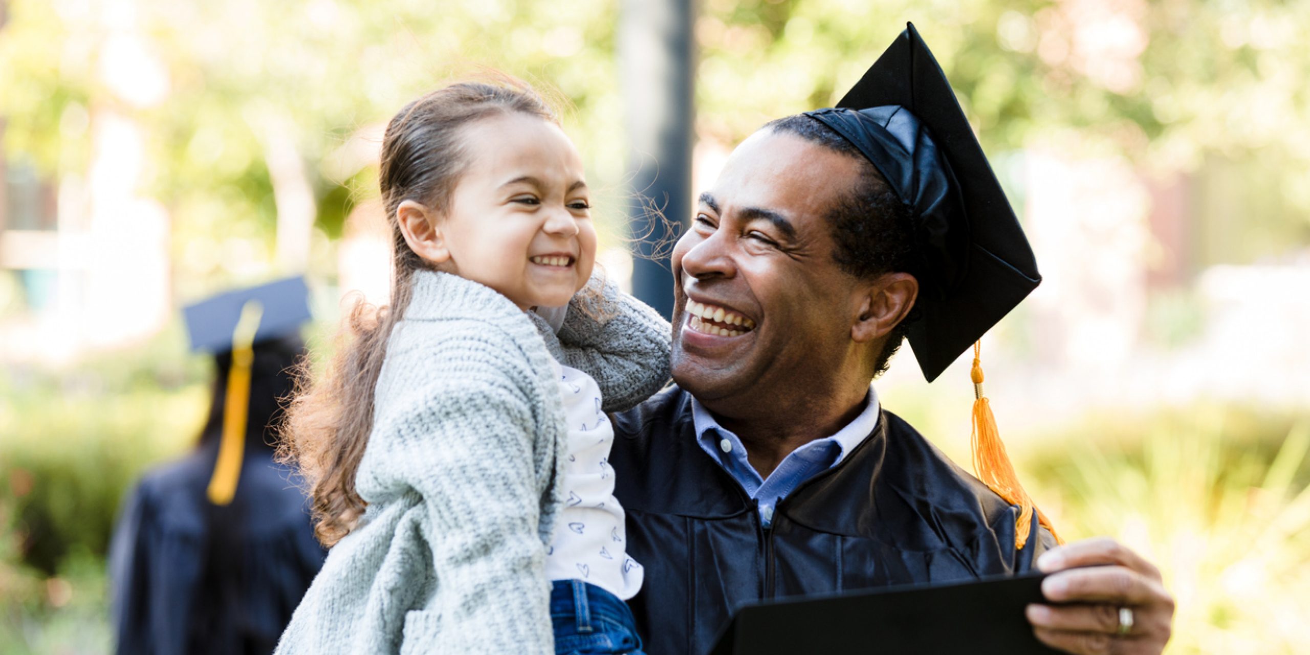 The little preschool age girl makes a silly face.  Her mature adult grandfather smiles and laughs.  He has just graduated.